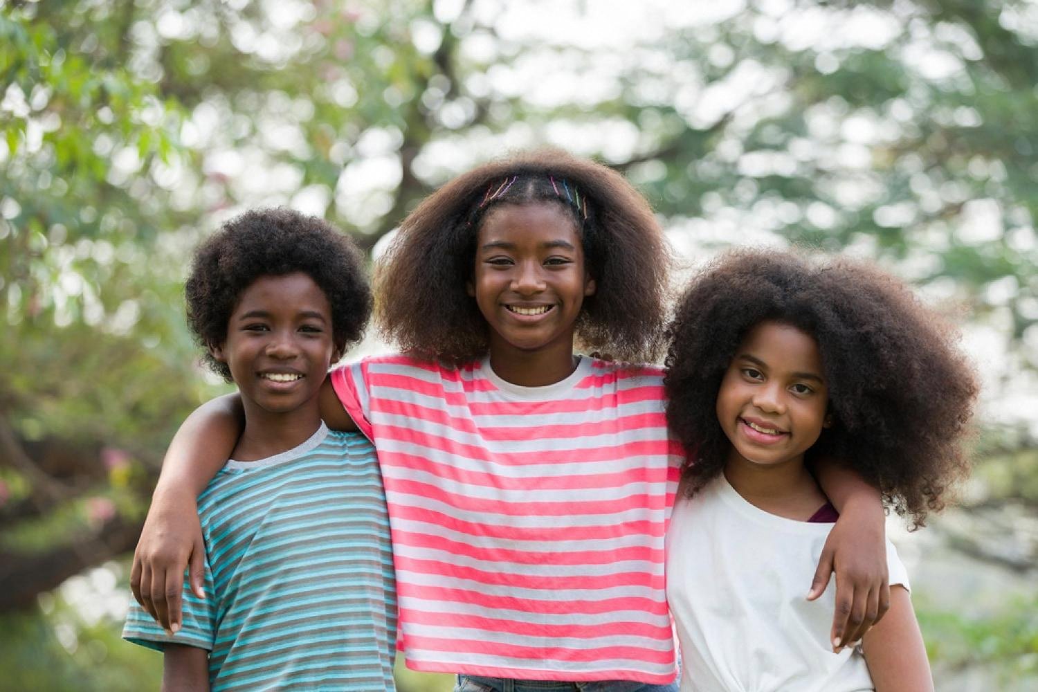 Three smiling students standing together on a school outing surrounded by greenery